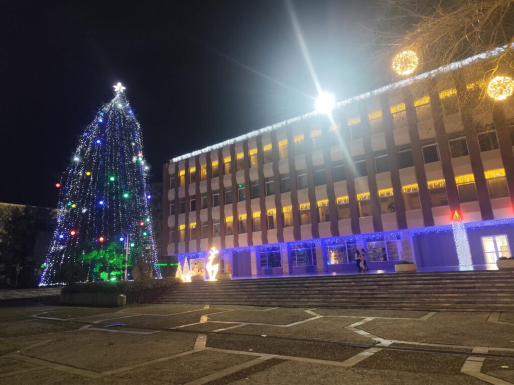 Осветена коледна елха пред сграда нощем